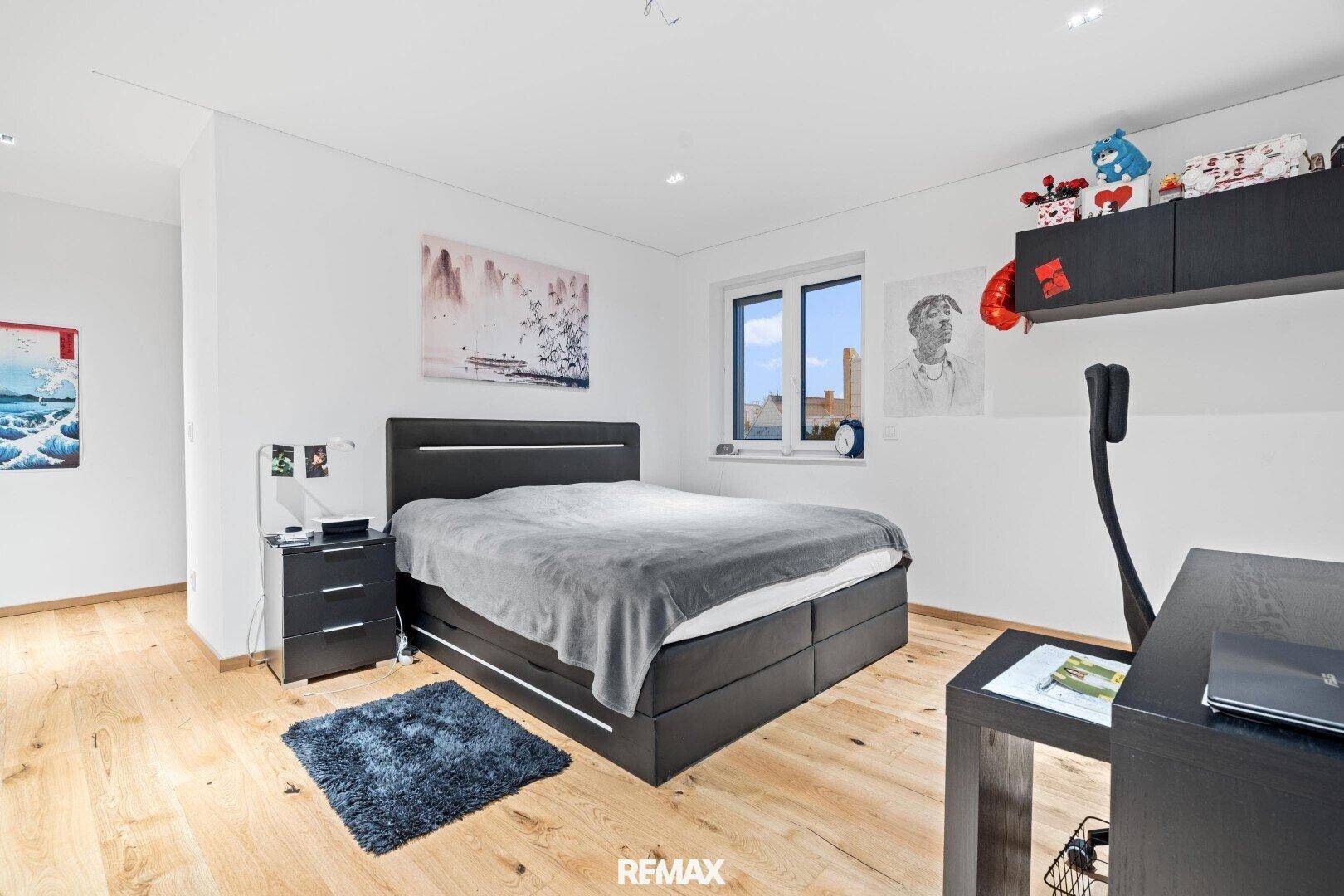 Helles Schlafzimmer mit Doppelbett, Schreibtisch und Holzboden, ideal für Arbeit und Entspannung.