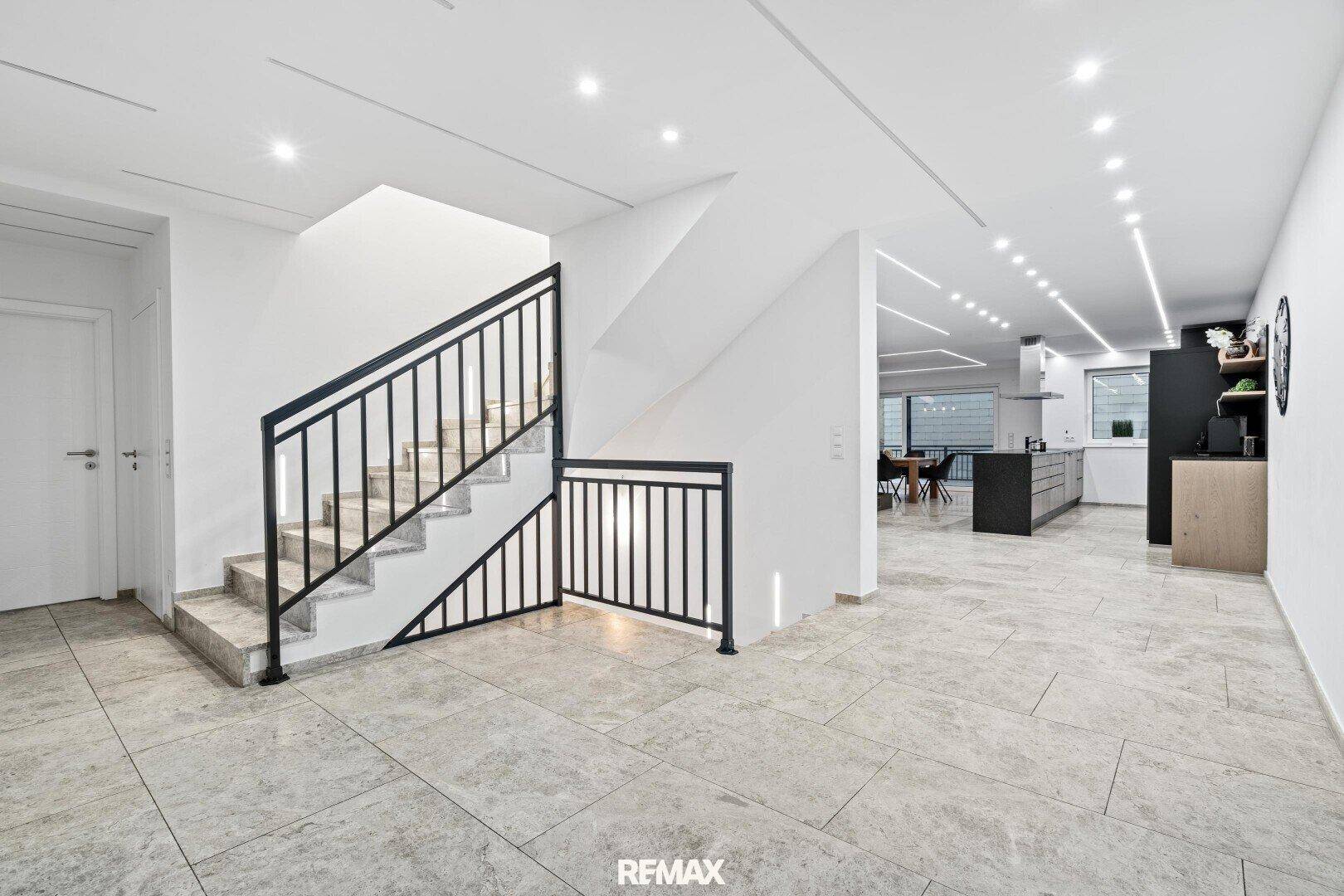 Heller Eingangsbereich mit moderner Treppe und offenem Zugang zum Wohn- und Küchenbereich.