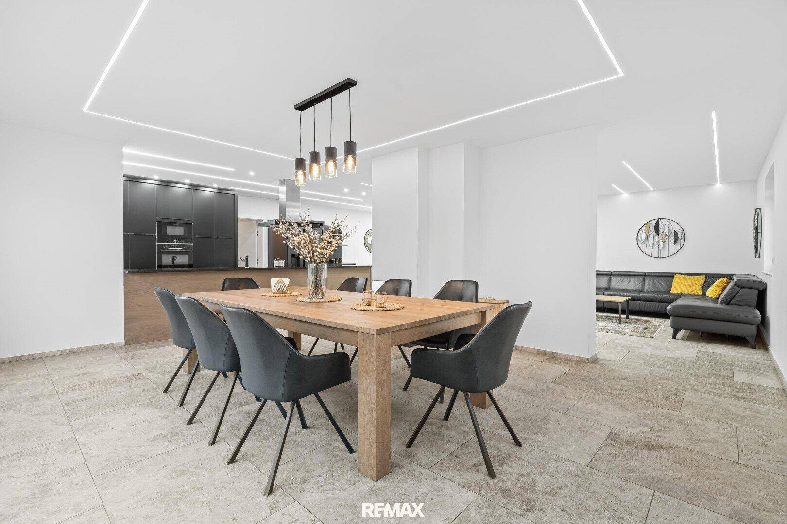 Heller Essbereich mit Holztisch und grauen Stühlen, offen zur modernen Küche und zum Wohnzimmer.