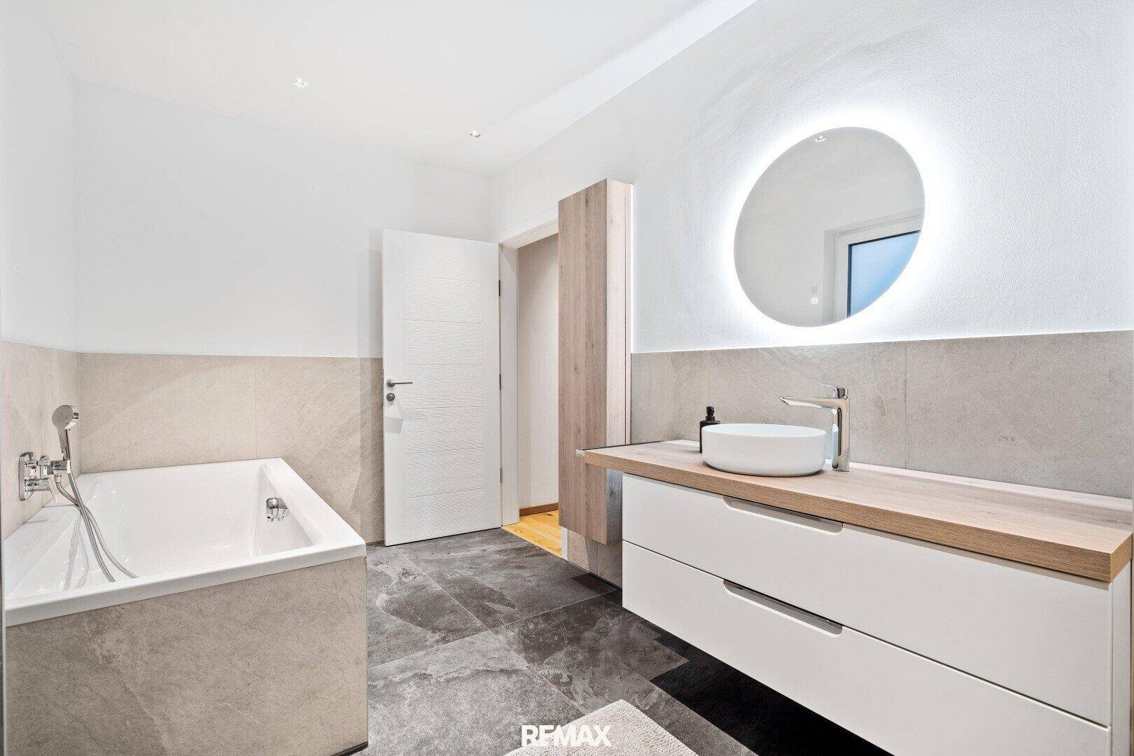 Modernes Badezimmer mit Badewanne, schwebendem Waschtisch und beleuchtetem Spiegel.