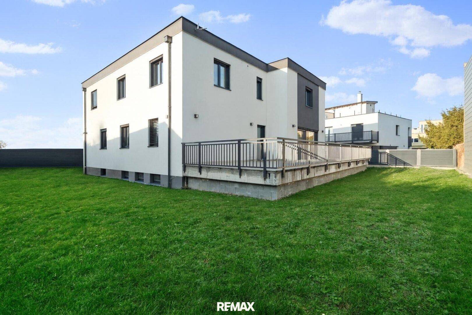 Rückansicht des Hauses mit großem Rasen und erhöhter Terrasse, ideal für Outdoor-Aktivitäten.