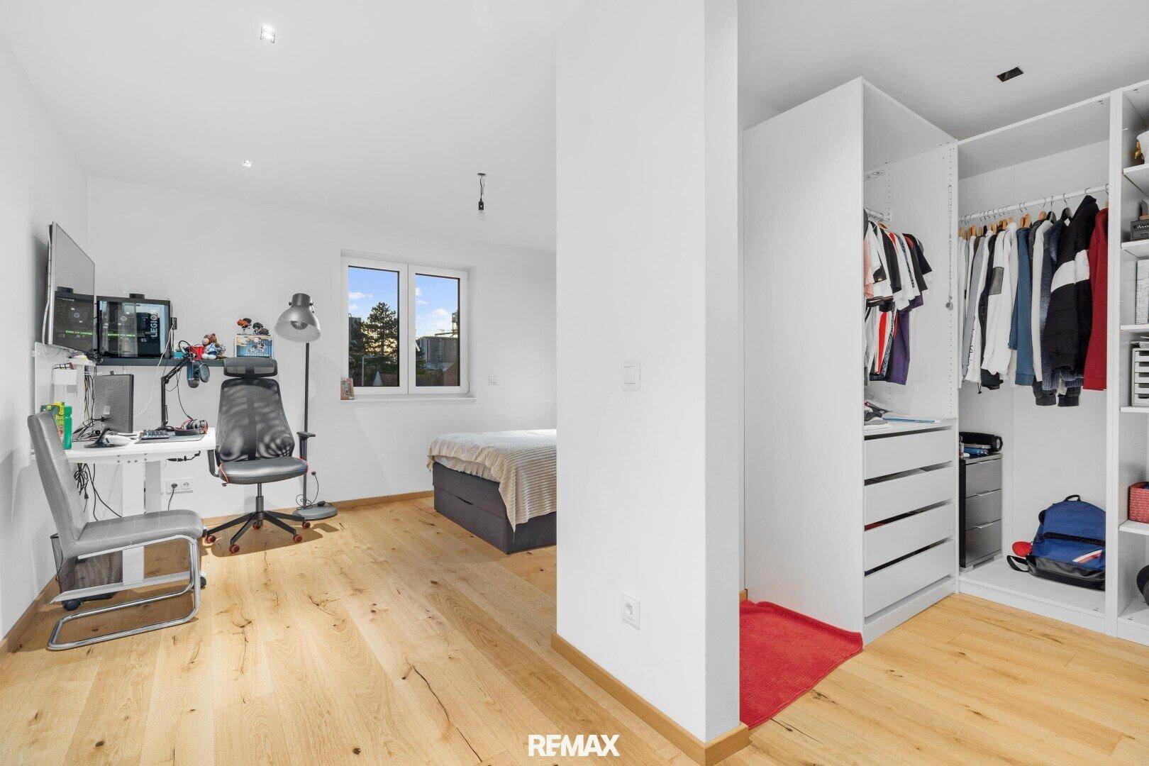 Schlafzimmer mit Bett, Schreibtisch und offenem Kleiderschrank, bietet vielseitige Nutzungsmöglichkeiten.