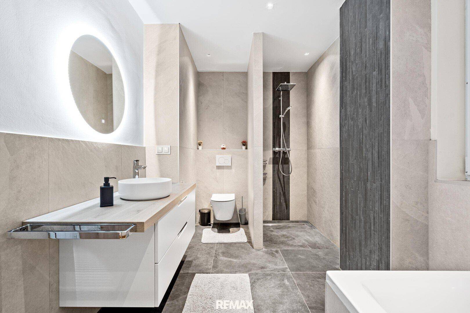 Modernes Badezimmer mit begehbarer Dusche, schwebendem Waschtisch und beleuchtetem Spiegel.