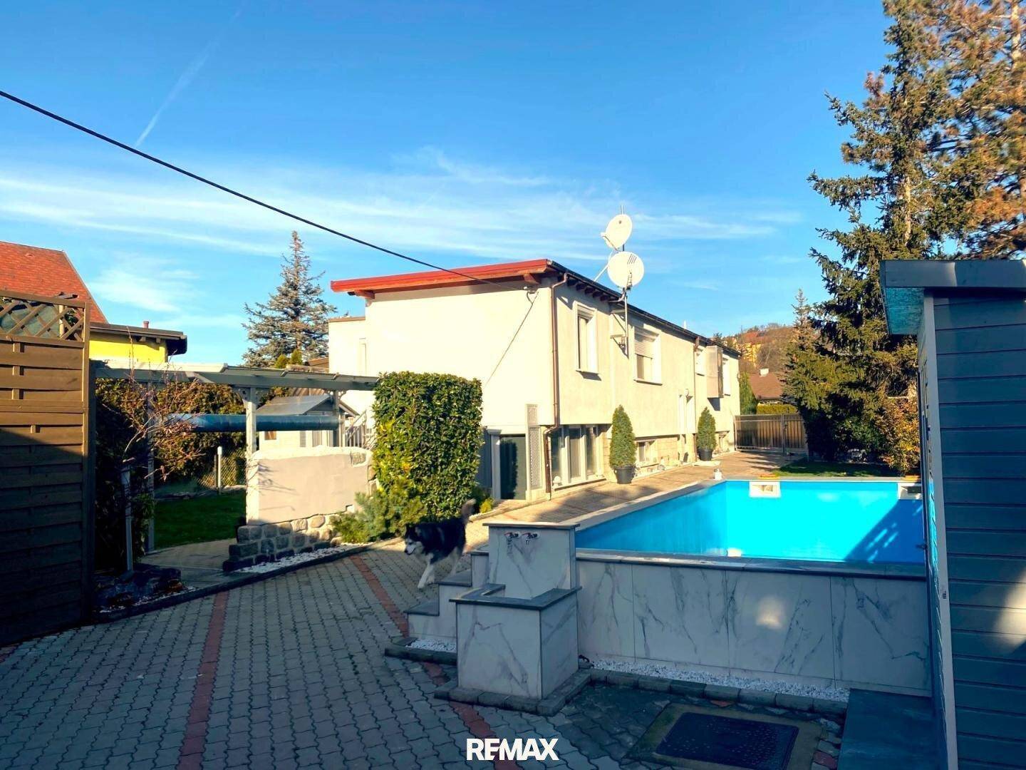 Seitenansicht des Hauses mit Swimmingpool und gepflegtem Außenbereich unter blauem Himmel.