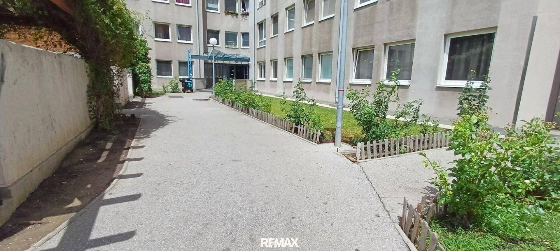 Eingangsbereich eines Mehrfamilienhauses mit gepflastertem Weg und kleinen Grünflächen.