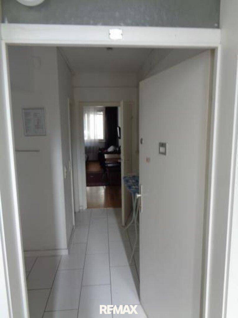 Heller Flur mit weißen Fliesen, der zu weiteren Räumen der Wohnung führt.