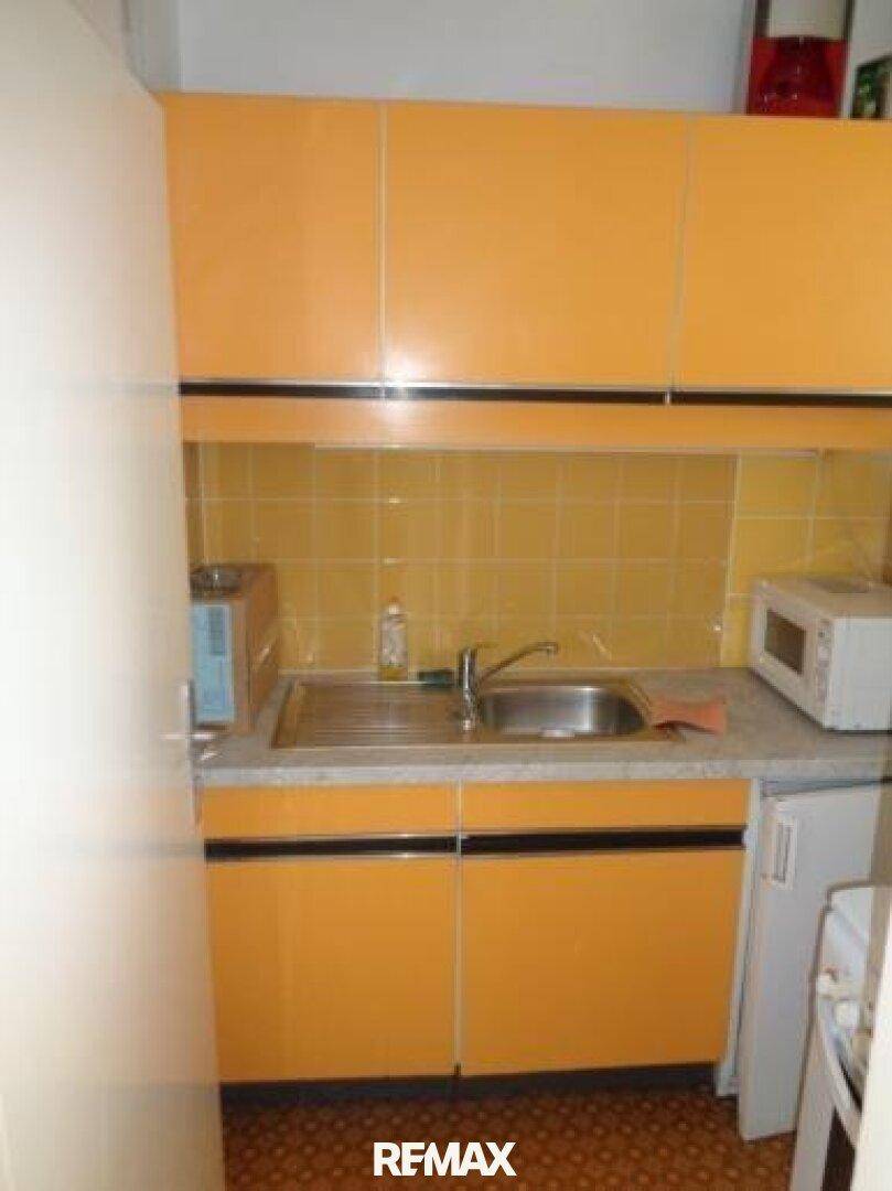 Kleine Küche mit orangefarbenen Schränken, gelben Fliesen und integrierter Spüle.