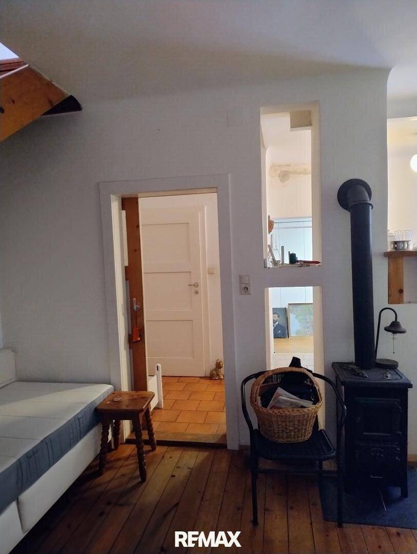 Wohnzimmer mit Holzofen, Sofa und Durchgang zu einem weiteren Raum mit Terrakottafliesen.