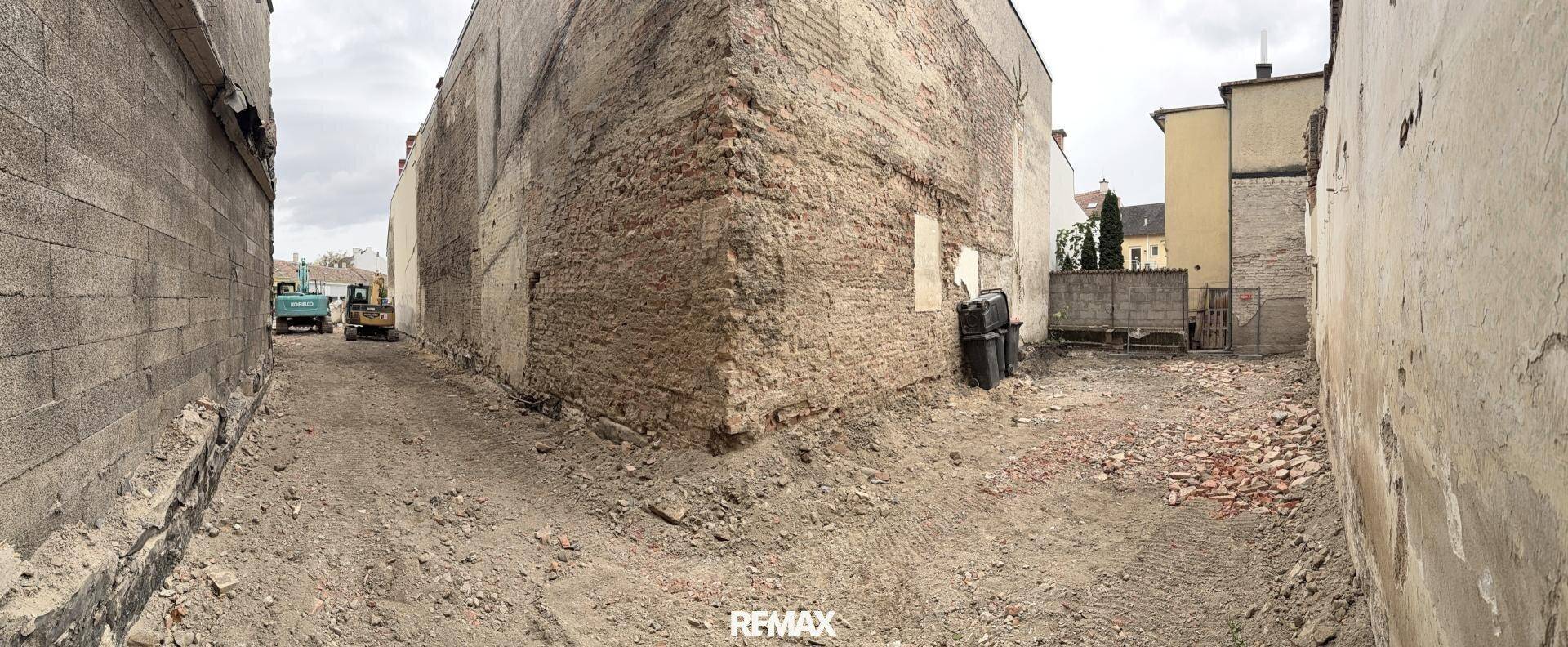 Freigelegte Baustelle zwischen zwei Gebäuden mit sichtbaren Ziegelwänden und Erdboden.