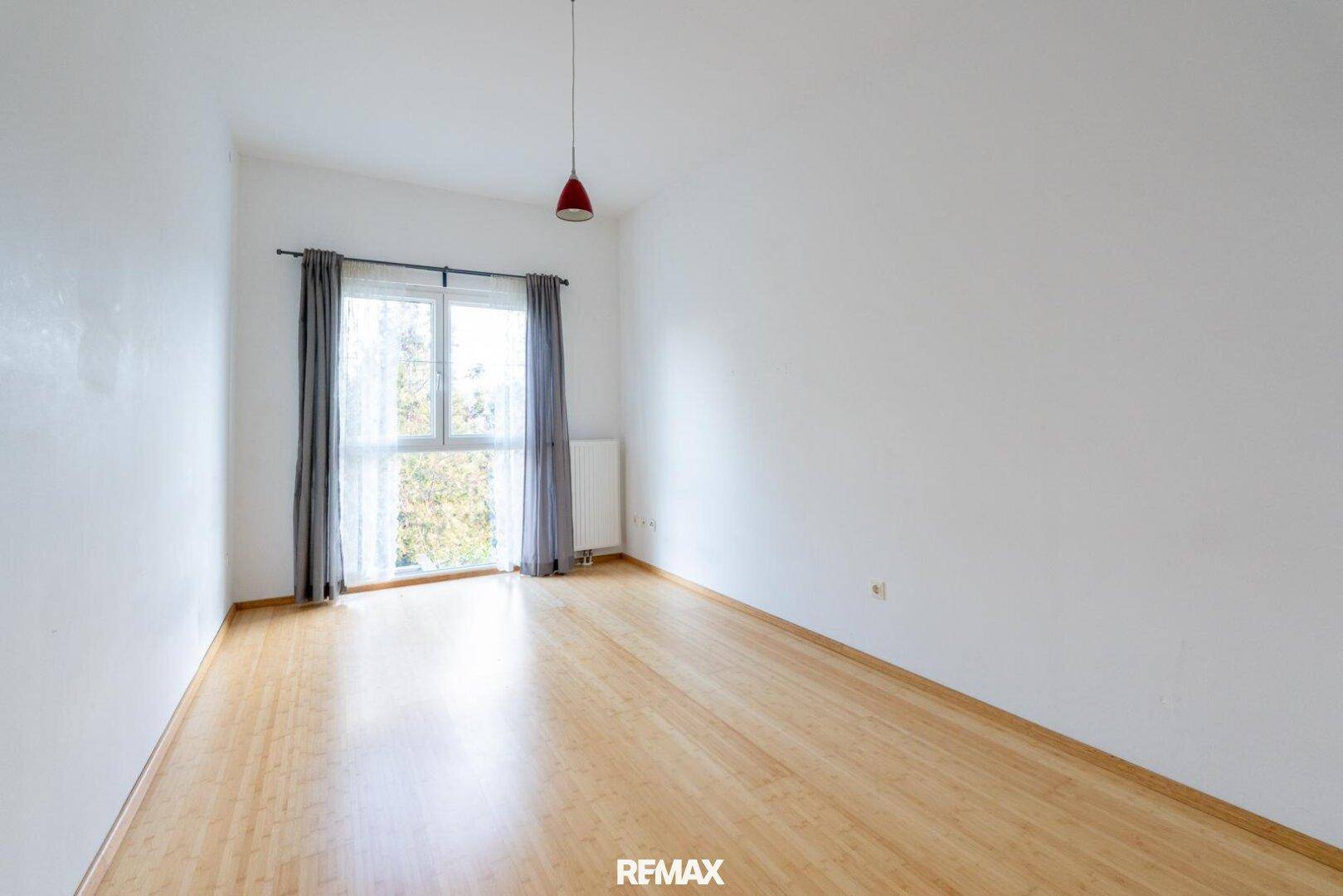 Helles Zimmer mit Holzfußboden und Fenster, das viel Tageslicht hereinlässt.