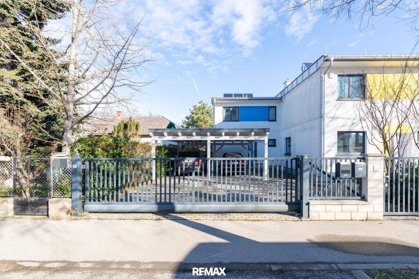 Vorderansicht des Hauses mit Zaun, Einfahrt und einem überdachten Carport für Fahrzeuge.