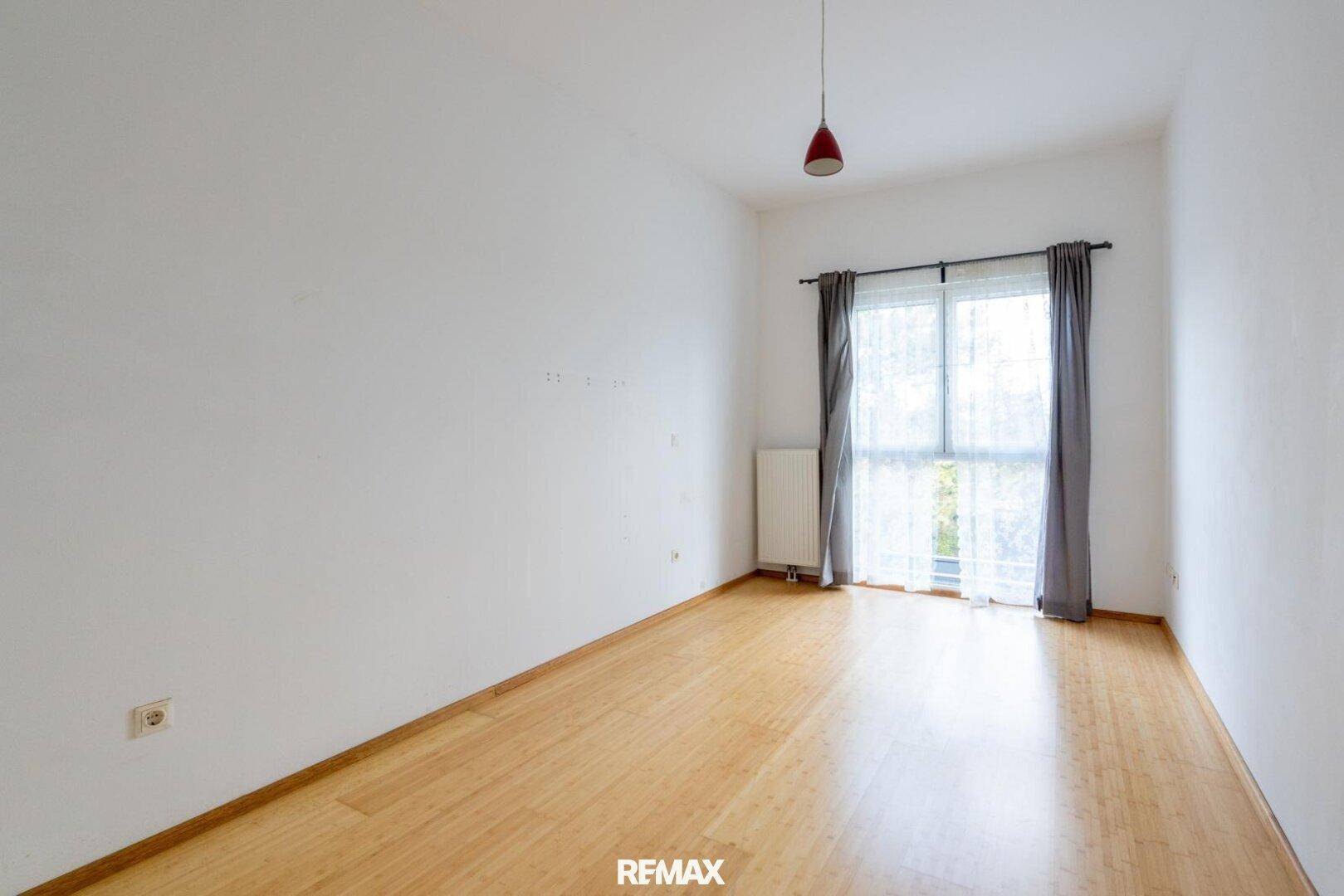 Helles Zimmer mit Holzfußboden und Fenster, das viel Tageslicht hereinlässt.