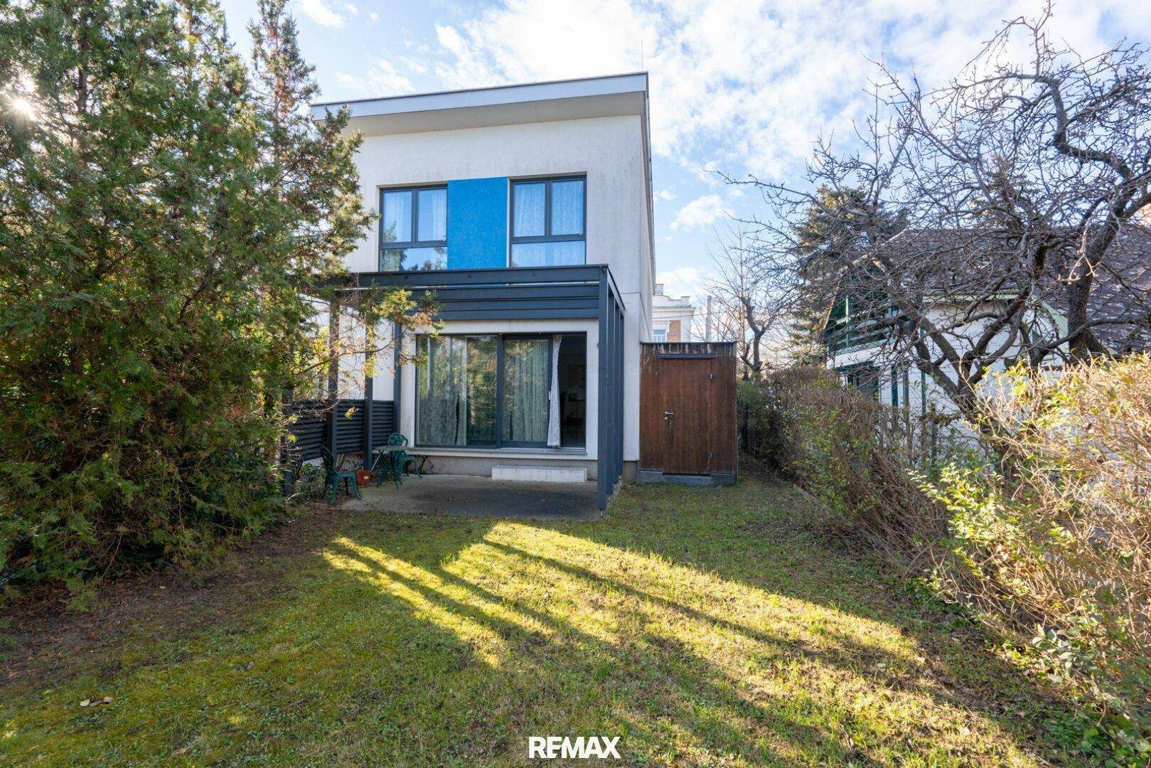 Rückseite des Hauses mit kleiner Terrasse und Rasenfläche, umgeben von Bäumen.