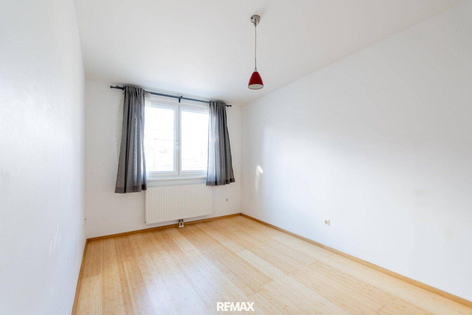 Helles Zimmer mit Holzfußboden und Fenster, das viel Tageslicht hereinlässt.