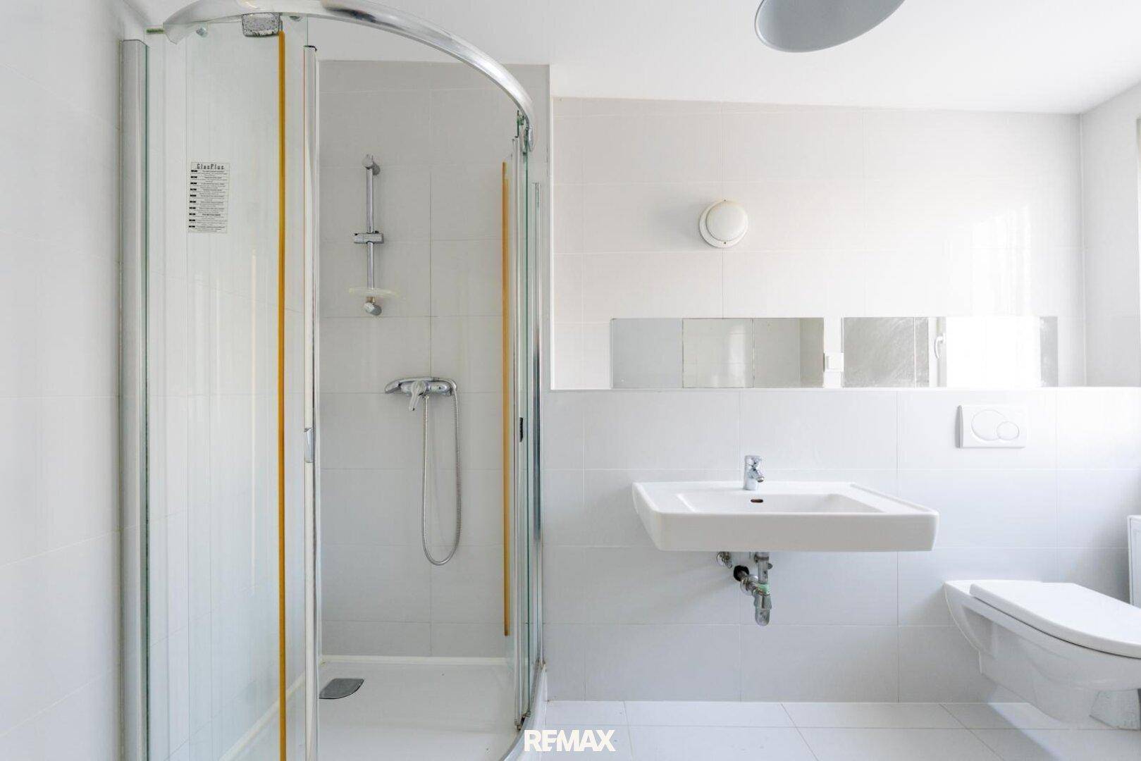 Modernes Badezimmer mit weiß gefliesten Wänden, Duschkabine, Waschbecken und Toilette.
