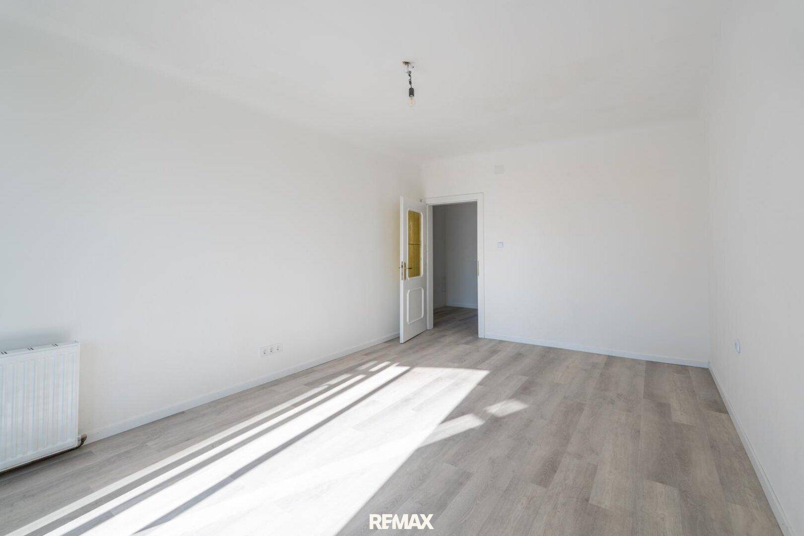 Geräumiges, helles Zimmer mit Laminatboden und viel natürlichem Tageslicht.