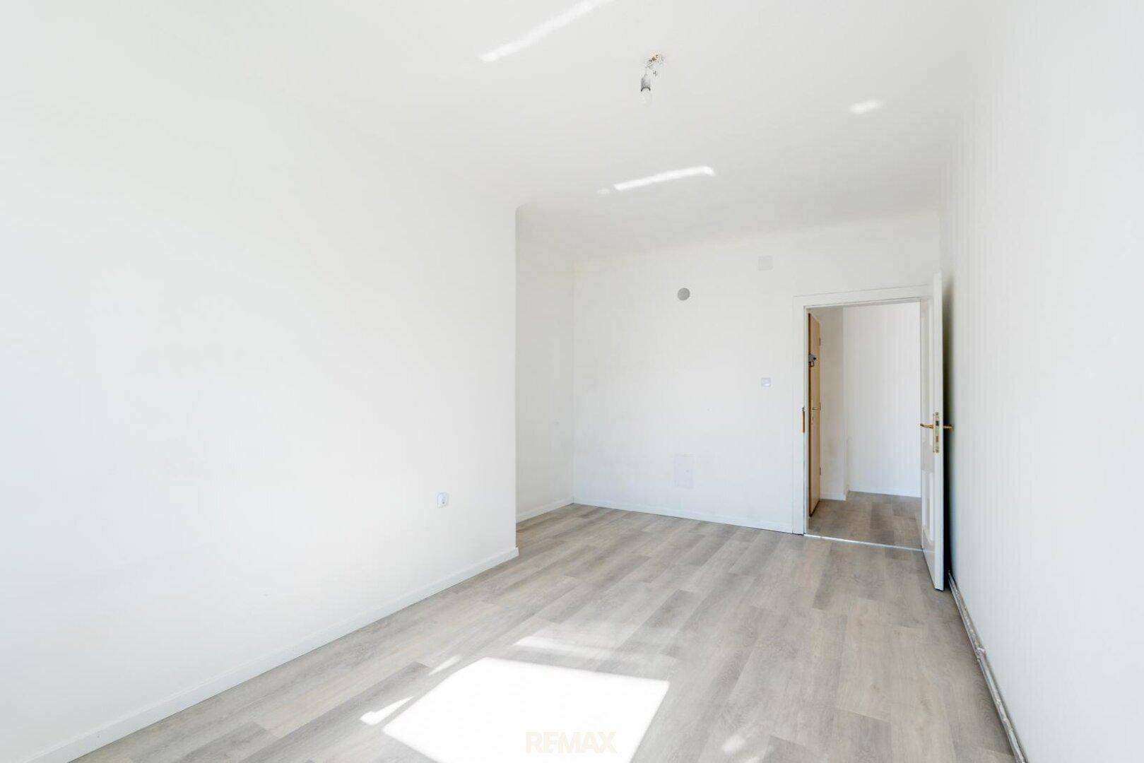 Helles, leeres Schlafzimmer mit Laminatboden und viel natürlichem Tageslicht.