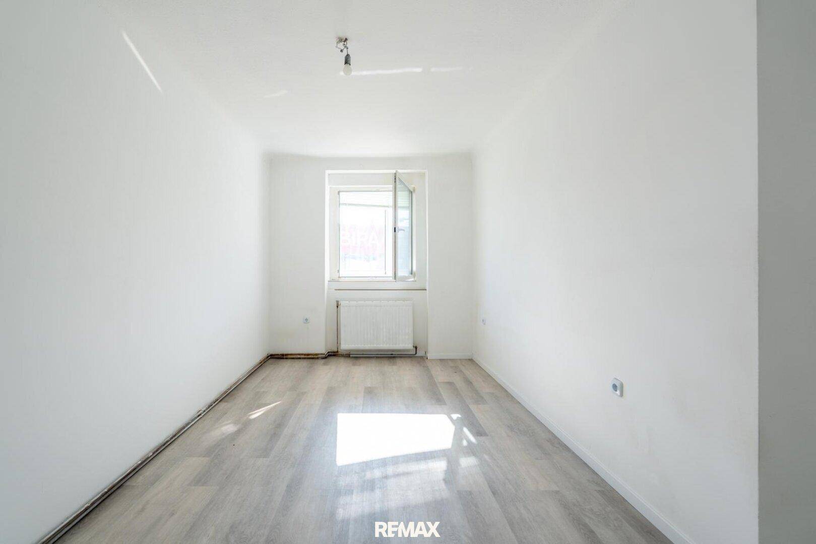 Helles Schlafzimmer mit Laminatboden und einem Fenster, das viel Licht hereinlässt.