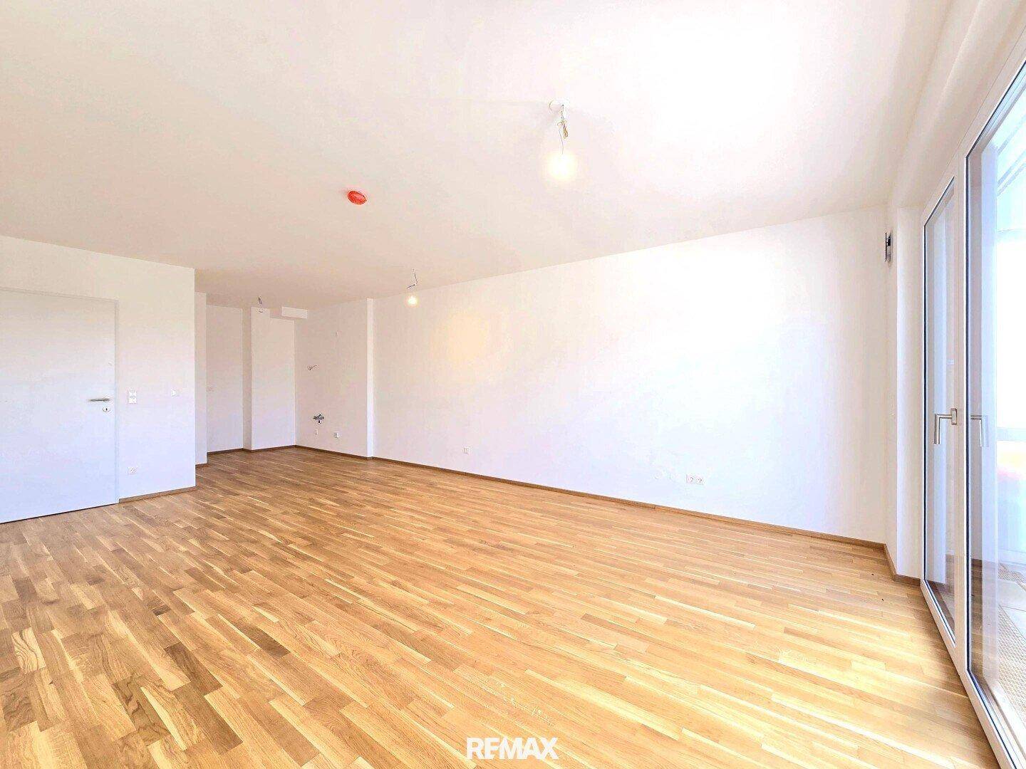 Geräumiger, unmöblierter Wohn-Essbereich mit Holzboden und Balkonzugang.