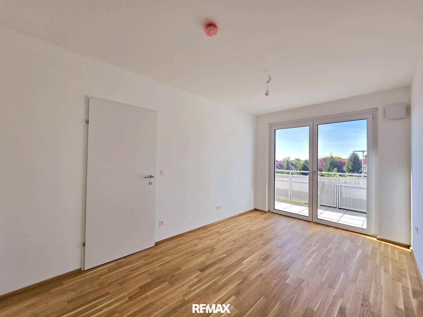 Unmöbliertes Schlafzimmer mit Holzboden und Zugang zum Balkon.