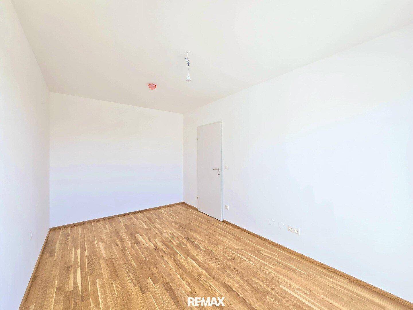 Leeres Schlafzimmer mit Holzboden und weißer Tür.