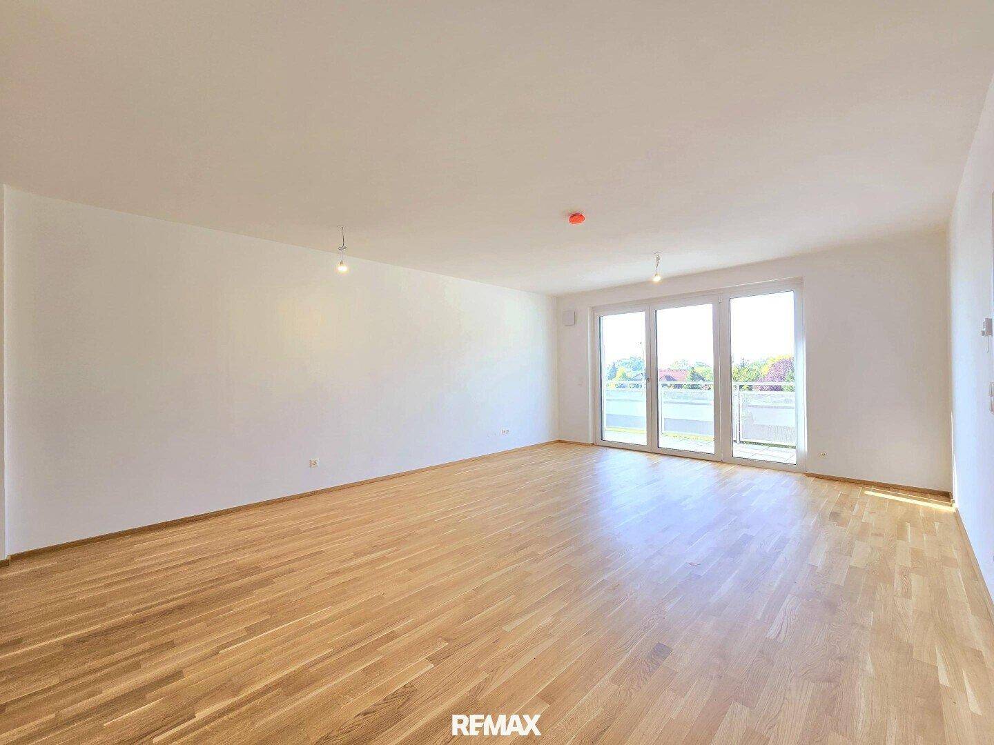 Geräumiger, leerer Wohn-Essbereich mit hellem Holzboden und Zugang zum Balkon.