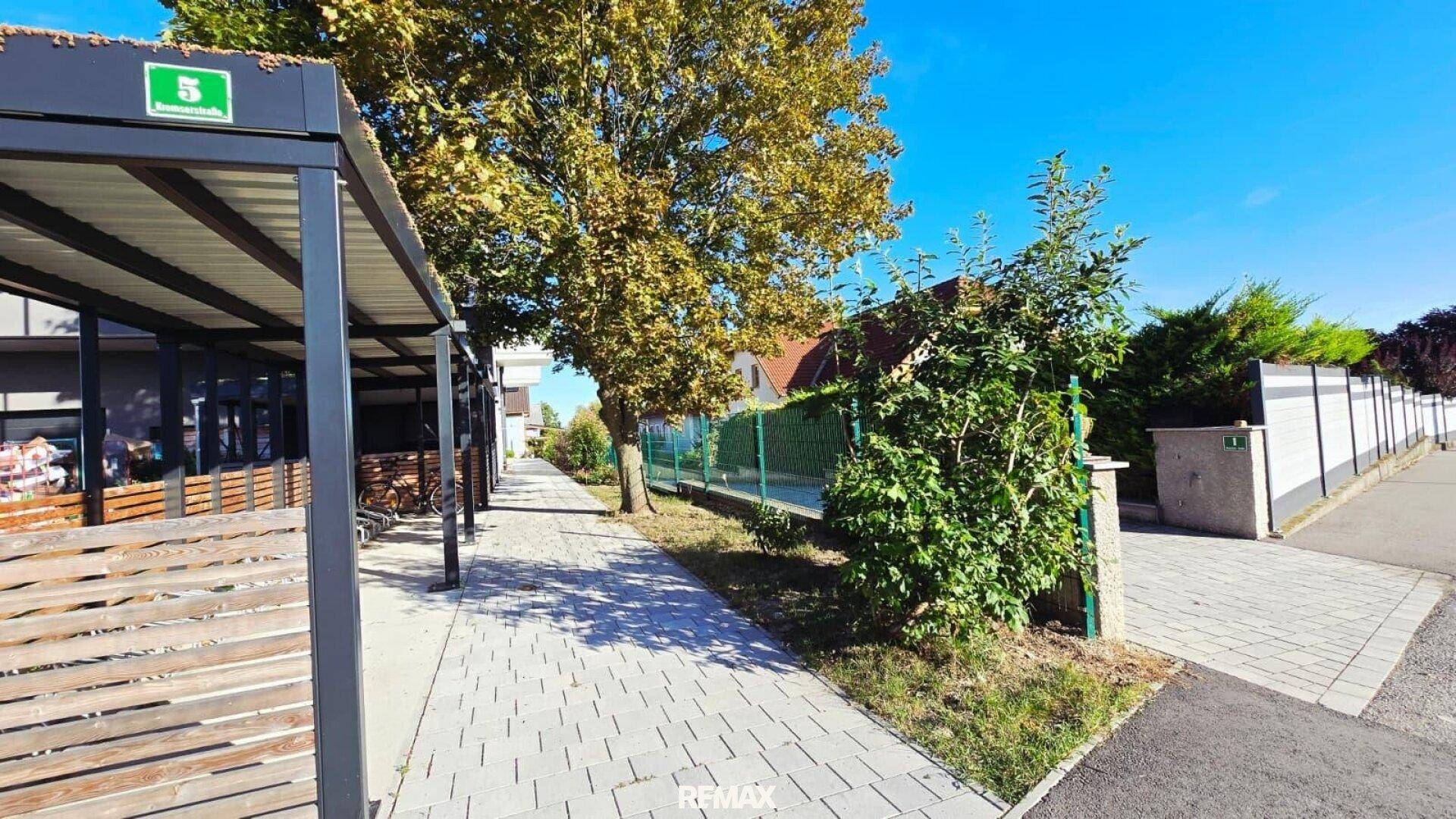 Gehweg entlang des Gebäudes mit Carports und Bäumen.