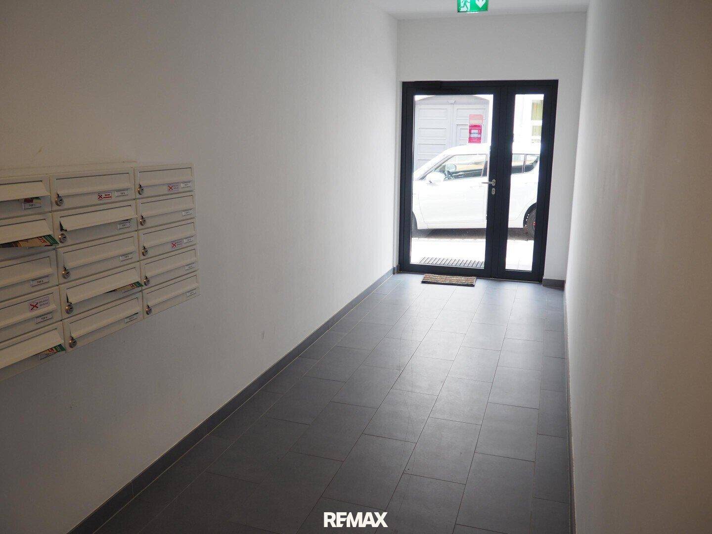 Heller Eingangsbereich mit Briefkästen, Fliesenboden und einer Glastür zum Außenbereich.