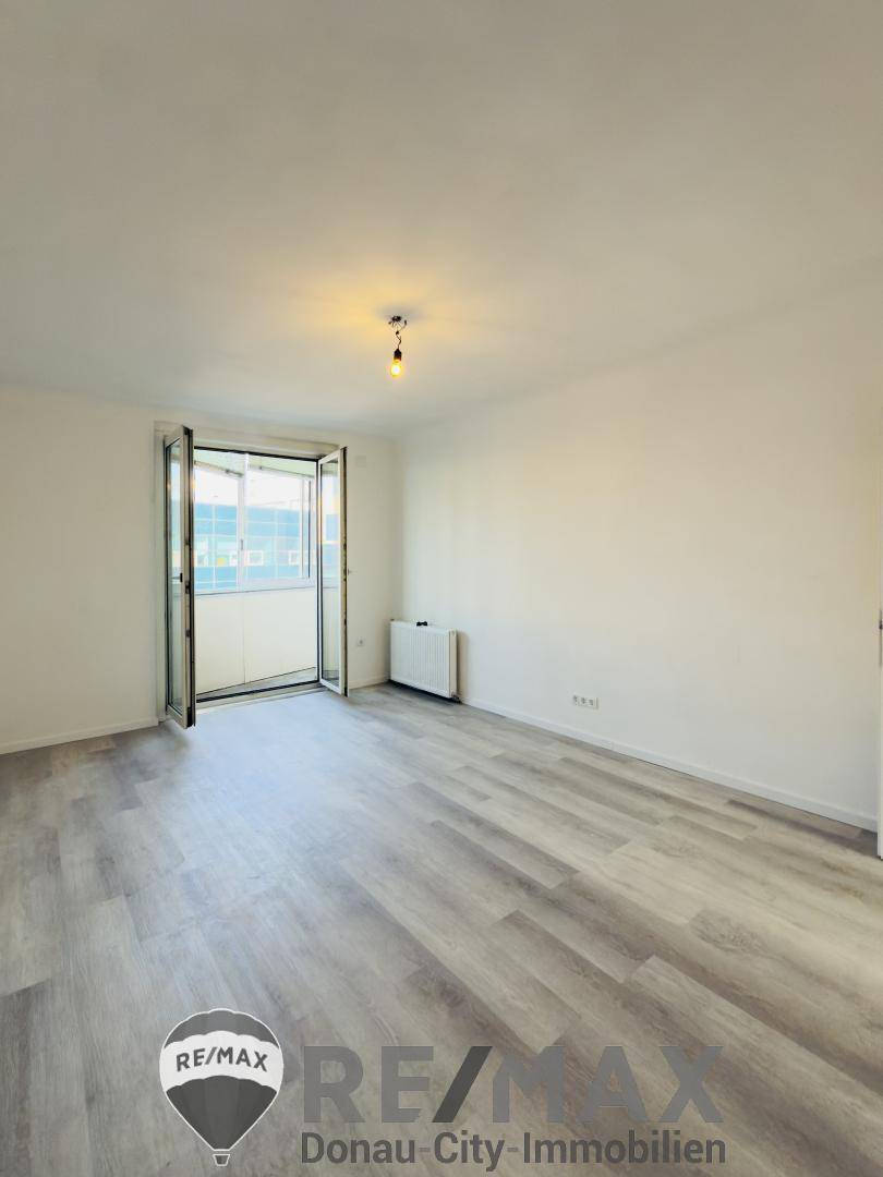 Leeres Wohnzimmer mit Laminatboden und direktem Zugang zu einem Balkon.