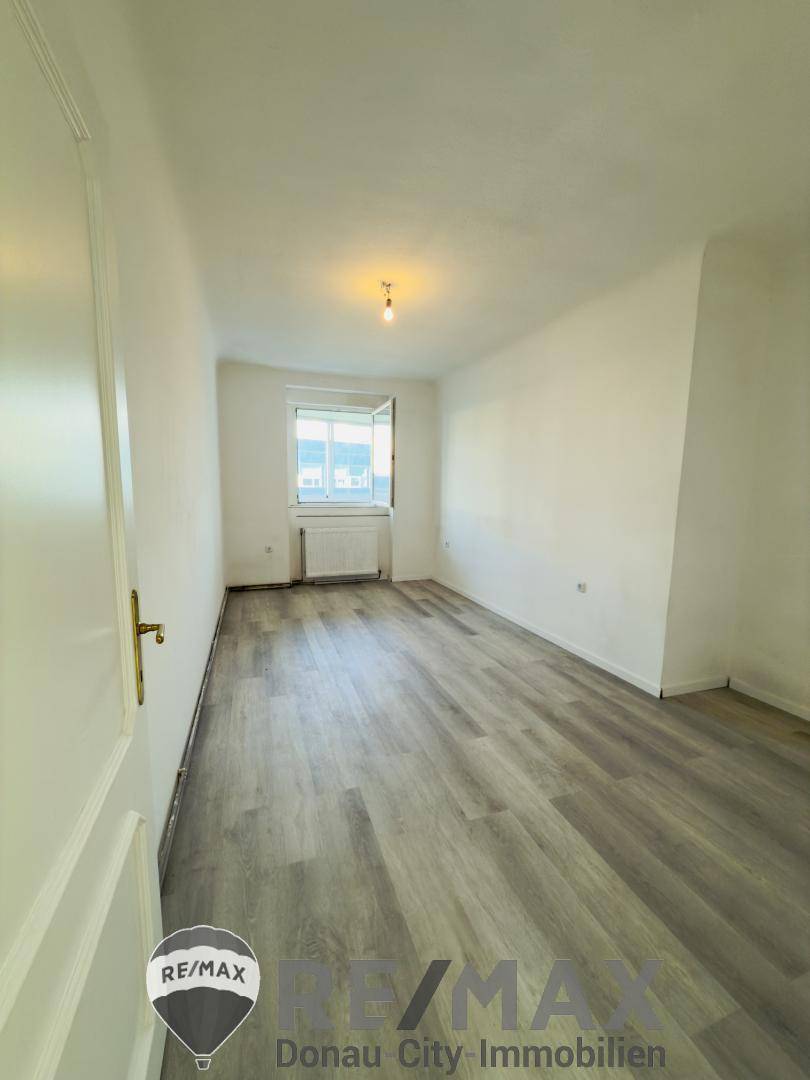 Leeres Schlafzimmer mit Laminatboden und Fenster, das auf eine Renovierung wartet.