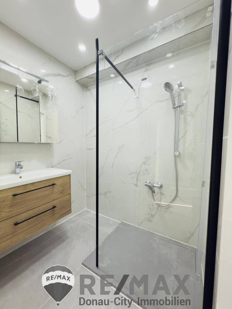 Modernes Badezimmer mit begehbarer Dusche, Waschtisch und eleganten Marmorfliesen.