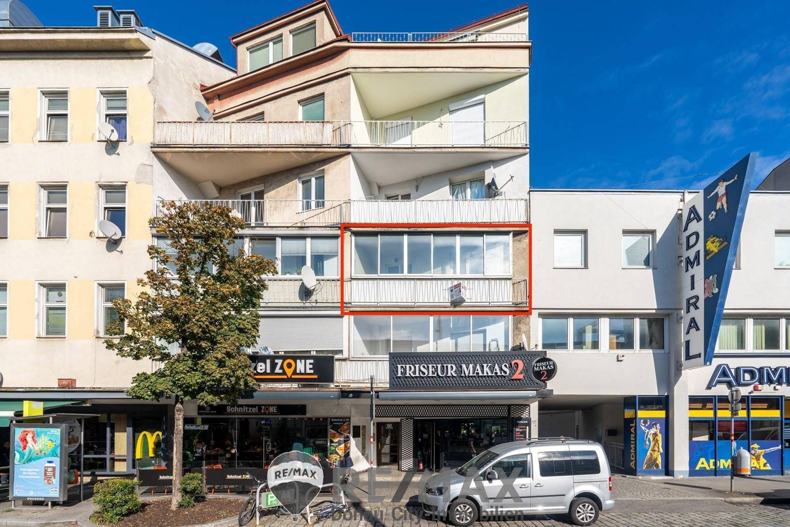 Städtisches Mehrfamilienhaus mit Geschäften im Erdgeschoss und Balkonen in der Fassade.