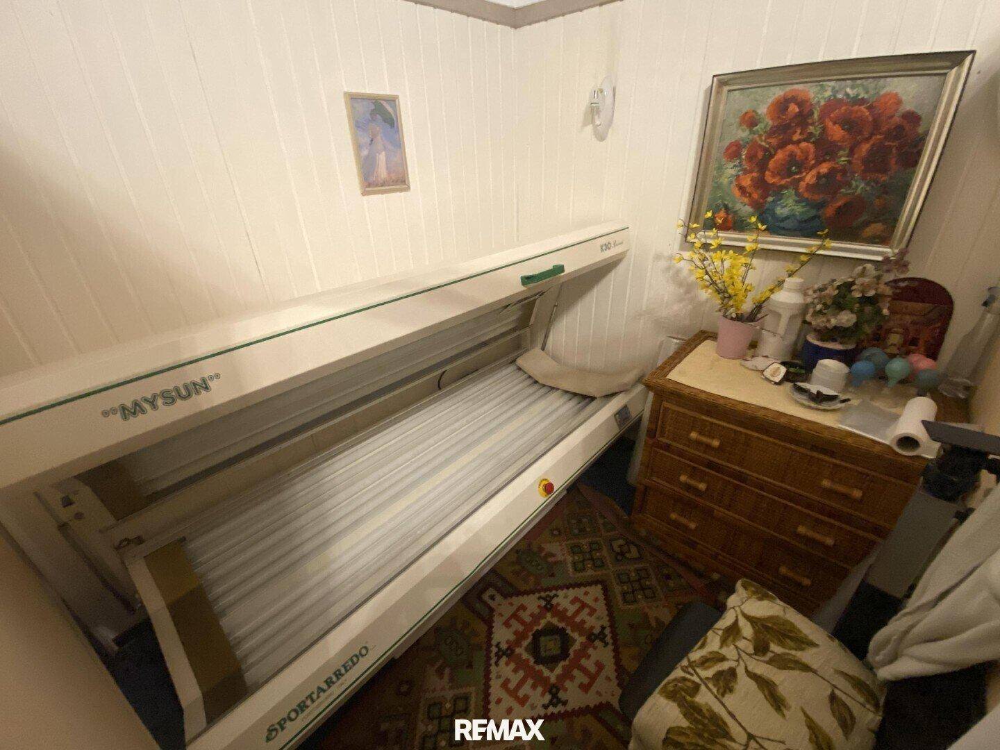 Raum mit einem Solarium, einer Holzkommode und einem gemusterten Teppich, für Entspannung und Bräunung.