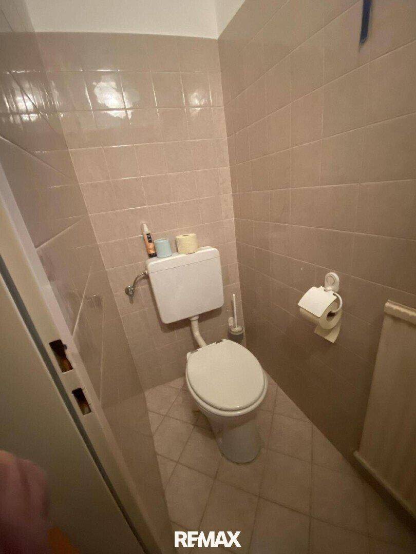 Separate Toilette mit beigefarbenen Fliesen und einfacher Ausstattung.