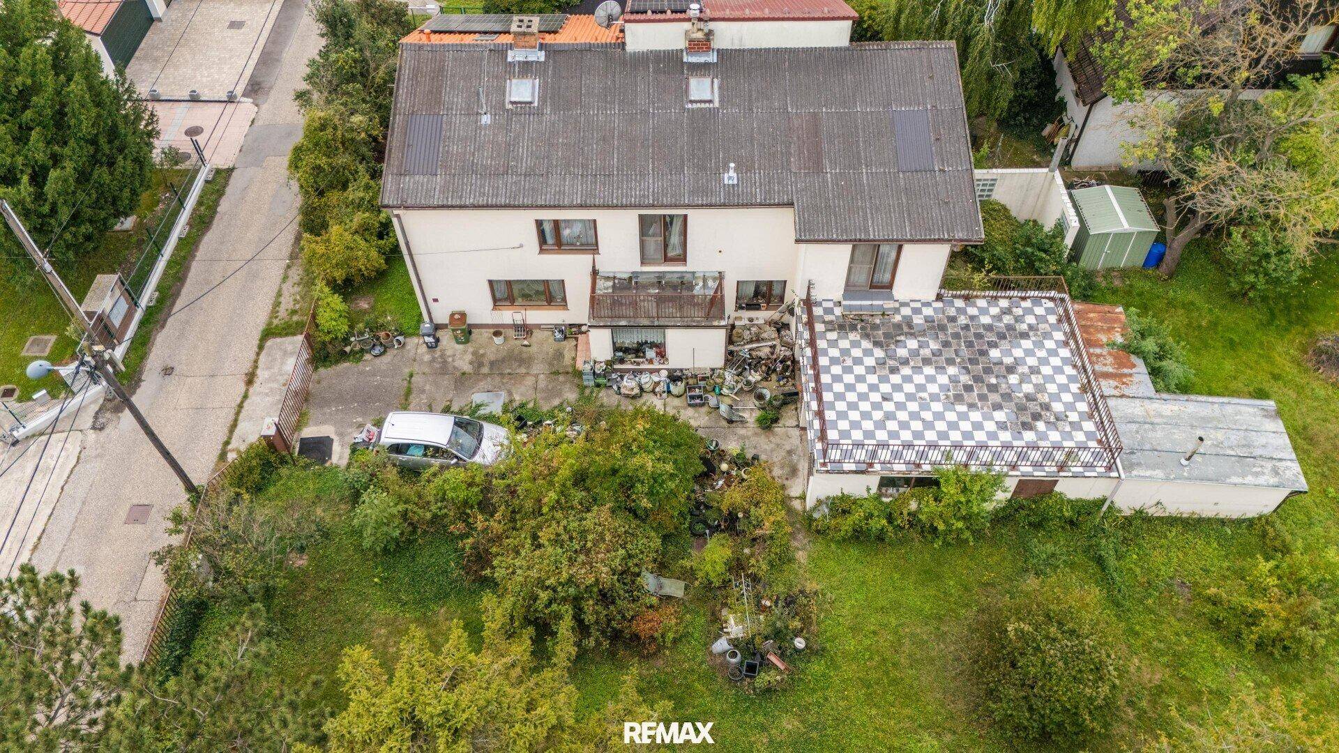 Rückansicht des Hauses mit kleinem Balkon und einer angrenzenden Struktur mit kariertem Dach.