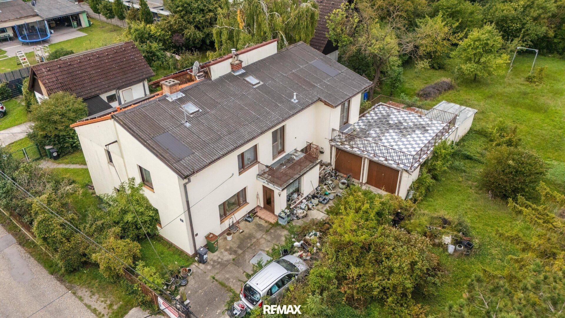 Vorderansicht des Hauses aus der Luft mit Zufahrt und dem umgebenden grünen Grundstück.