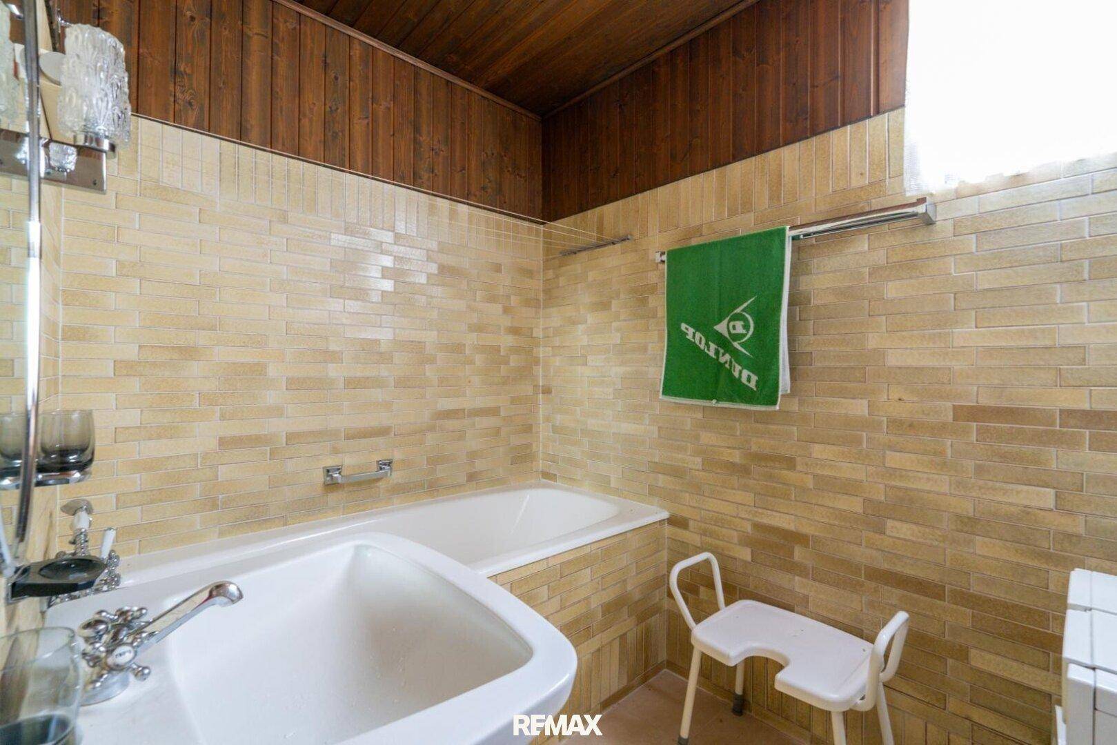 Badezimmer im 80er-Jahre-Stil mit beigen Fliesen, Badewanne und Holzdecke, funktional ausgestattet.