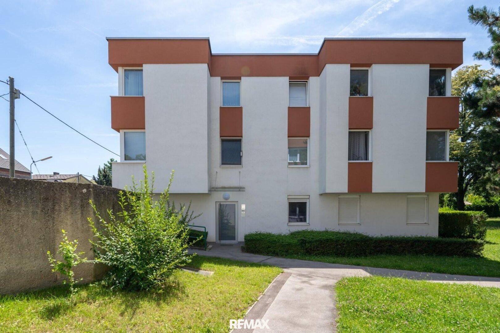 Modernes Mehrfamilienhaus mit weißer Fassade, braunen Elementen und Grünflächen, sehr gepflegt.