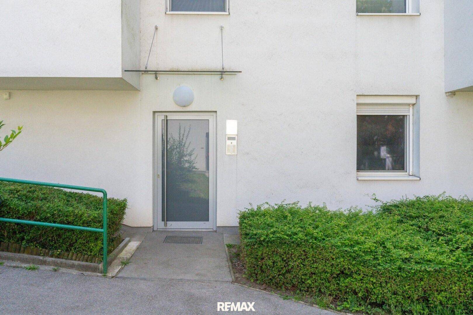 Eingangsbereich eines Mehrfamilienhauses mit Rampe für Barrierefreiheit und gepflegter Hecke.