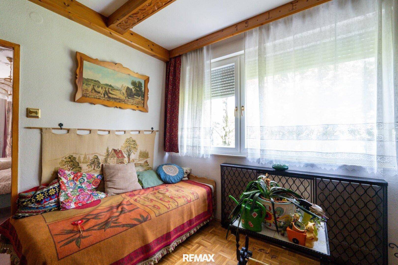 Gemütliches Zimmer mit Tagesbett, Holzbalken und Fenster mit Blick ins Grüne, sehr hell.