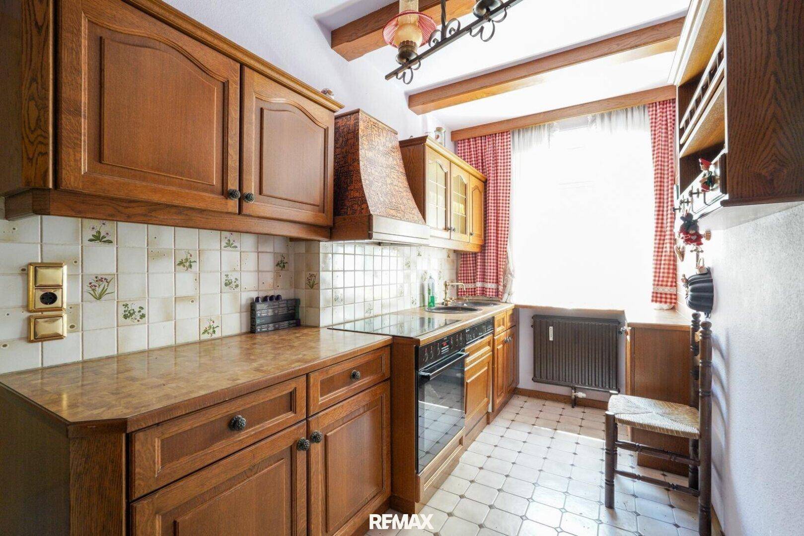 Traditionelle Holzküche mit karierten Vorhängen, Fliesenrückwand und integriertem Kochfeld am Fenster.
