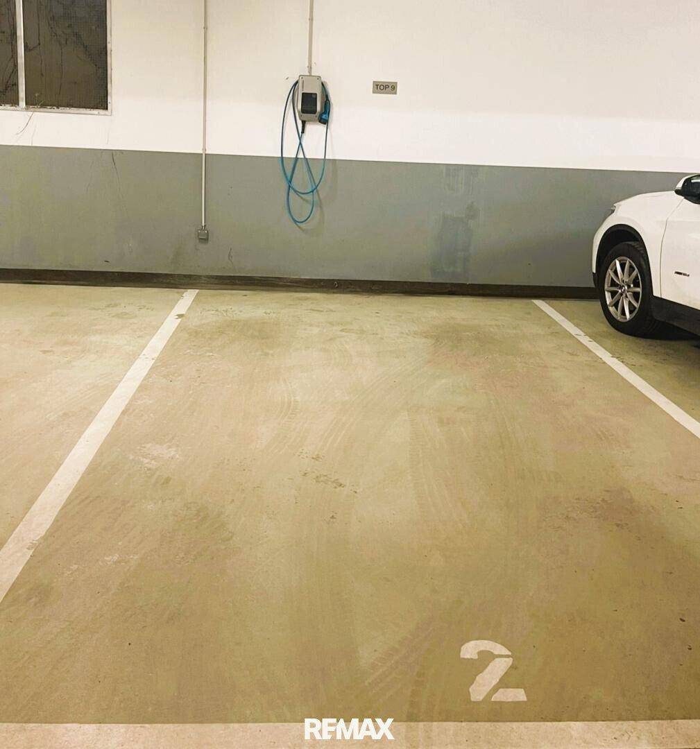 Zwei Tiefgaragenstellplätze, einer davon mit einem weißen Auto und einer Ladestation.