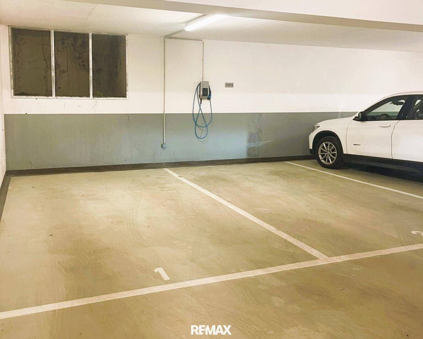 Tiefgaragenstellplatz mit Elektroauto-Ladestation und einem geparkten weißen Fahrzeug.