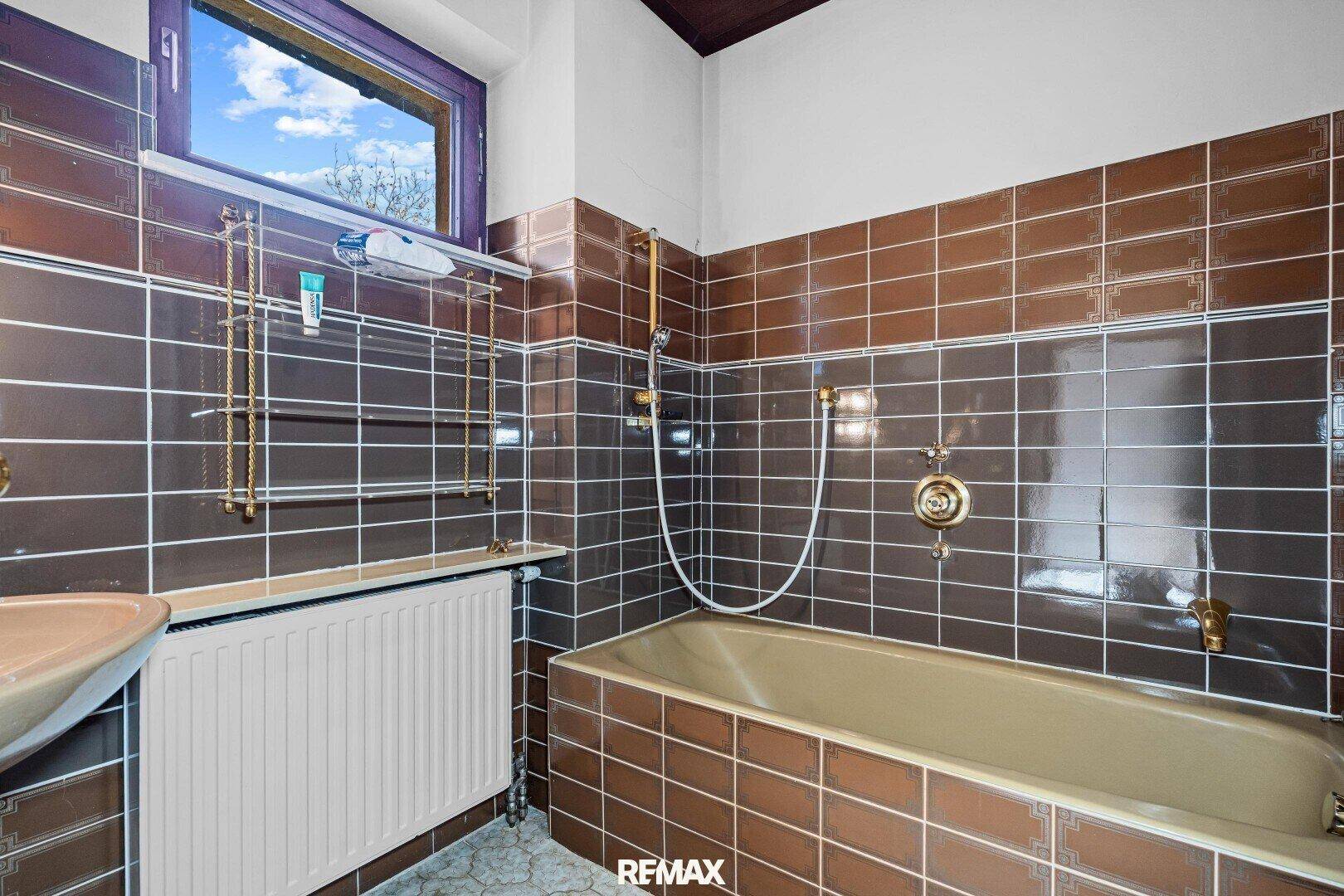 Badezimmer mit braunen Fliesen, Badewanne und einem Fenster für natürliche Belüftung.