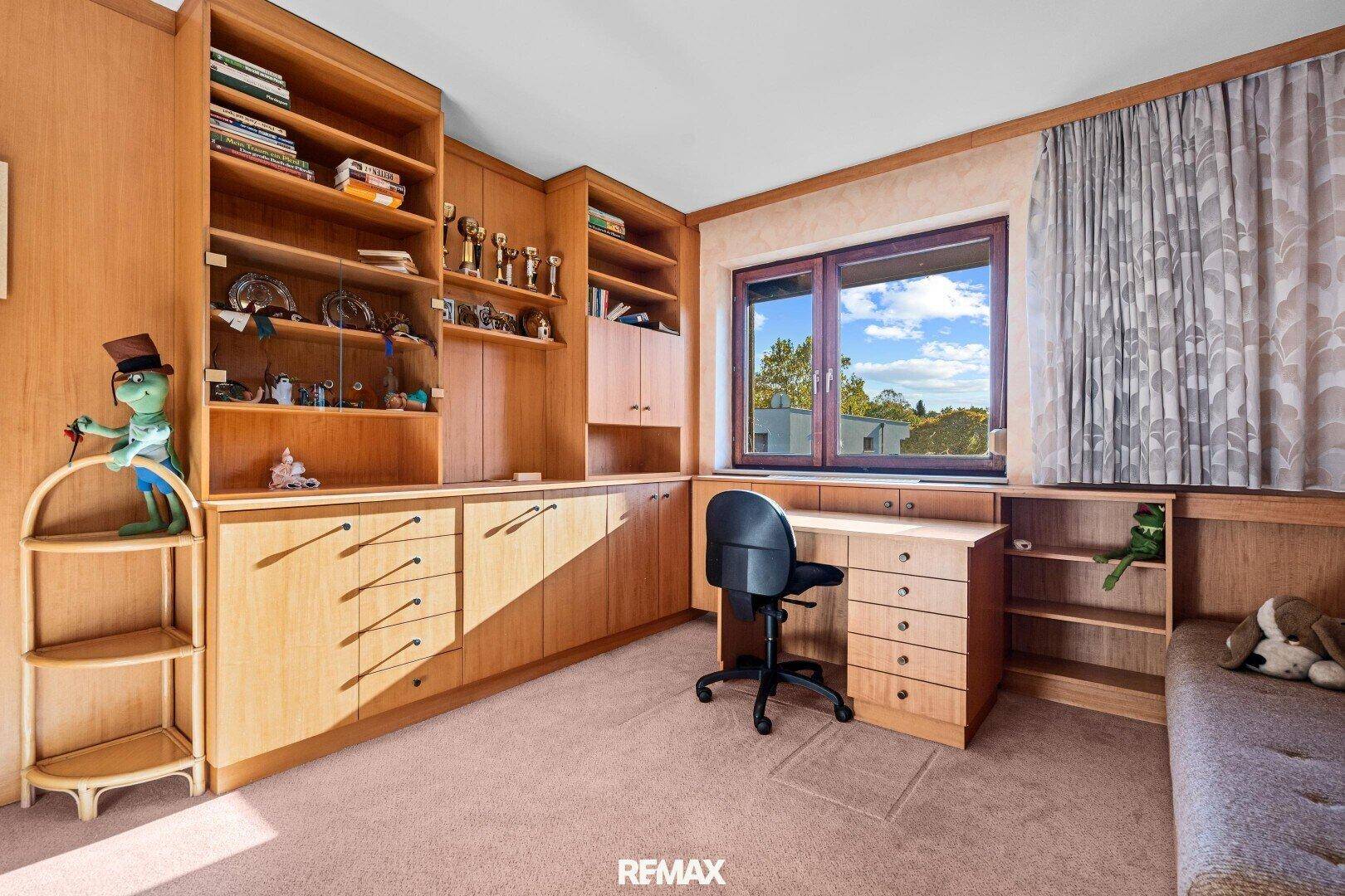 Arbeitszimmer mit maßgefertigten Holzregalen, Schreibtisch und Teppichboden.