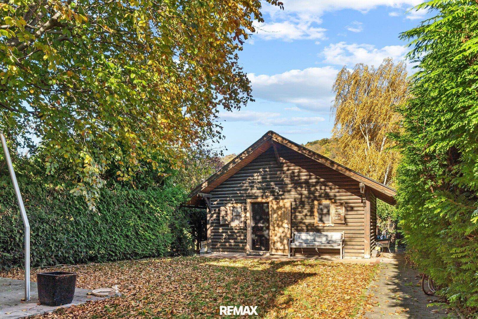 Rustikale Holzhütte im Garten, umgeben von Bäumen und herbstlichem Laub.