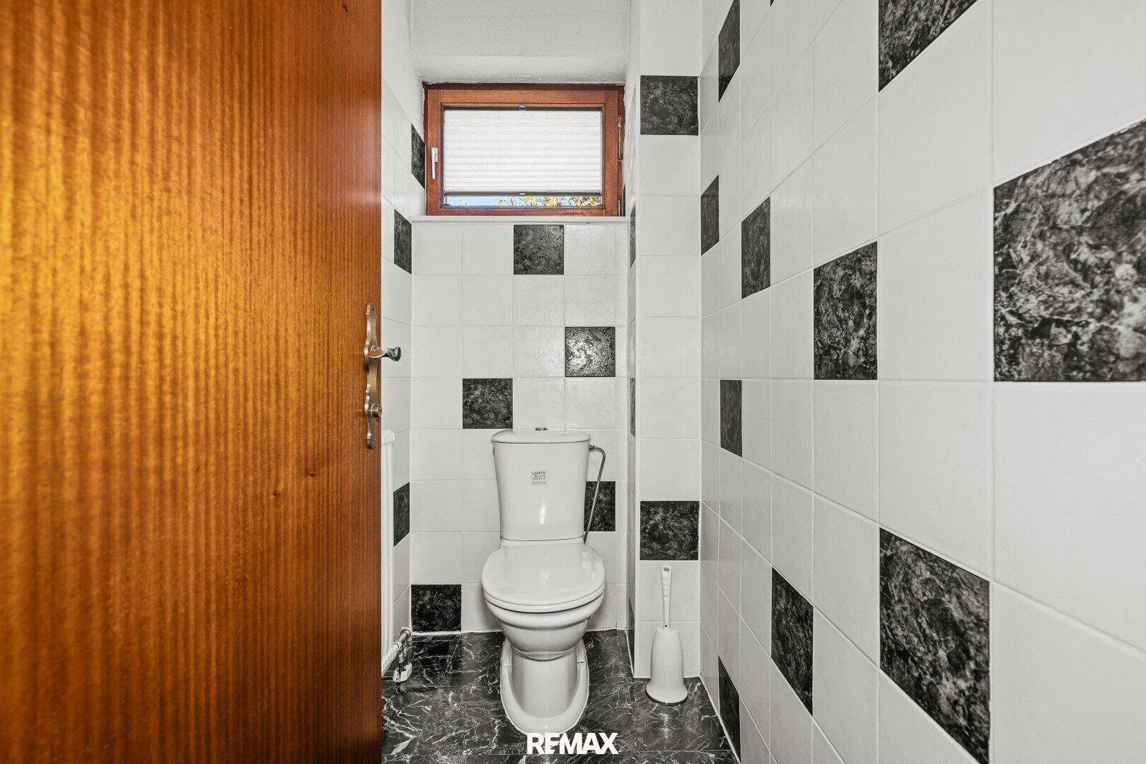 Kleines WC mit schwarz-weißen Fliesen und einem Fenster für Tageslicht.