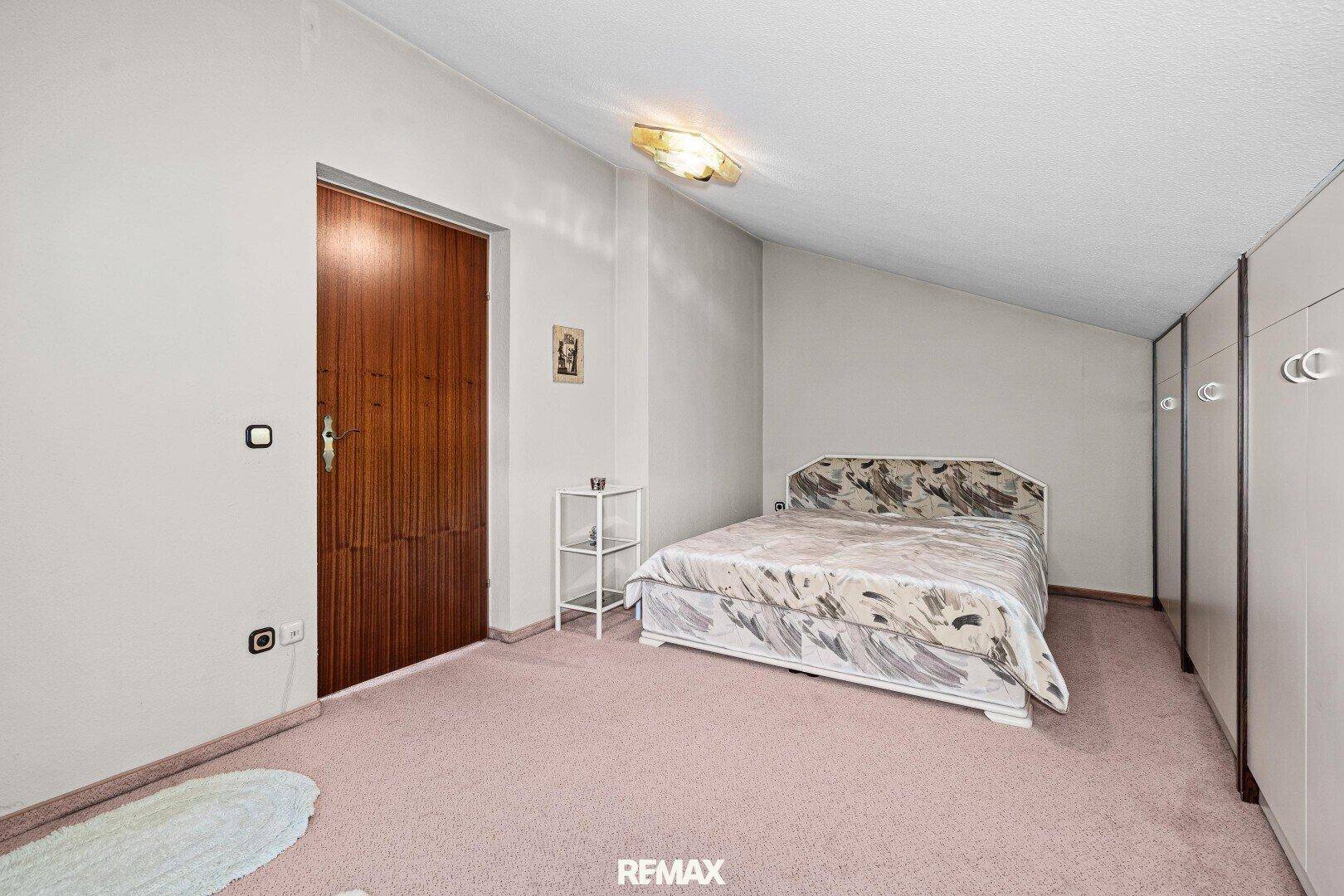 Schlafzimmer mit Dachschräge, rosa Teppichboden und praktischen Einbauschränken.