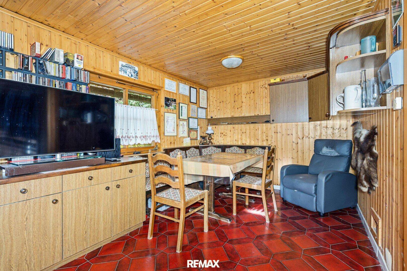 Innenraum der Holzhütte mit Holzvertäfelung, Essbereich und rustikalem Fliesenboden.