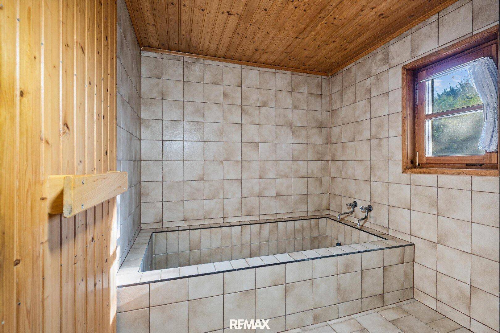 Badezimmer in der Holzhütte mit gefliesten Wänden und einer eingebauten Badewanne.